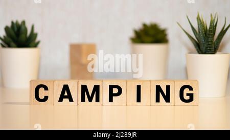 Camping-Wort auf einem Holzwürfelschild mit verschwommenem Hintergrund eines Campingplatzes im Sommer. Stockfoto