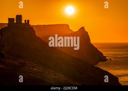 Ein rot brennender Sonnenuntergang mit dem Silhouett einer Klippe Und Burg über dem Meer Stockfoto