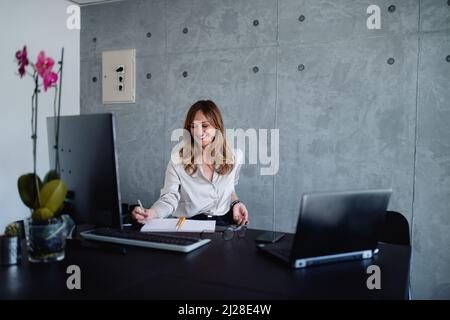 Ein braunhaariger kaukasischer Journalist mittleren Alters erstellt einen Bericht über ein Treffen im Unternehmen. Sie mag auch eine angenehme Umgebung. Stockfoto