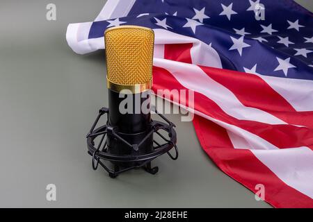 Schwarz-goldenes Studiomikrofon neben einer amerikanischen Flagge auf grünem Hintergrund. In diesem Zustand der Stille wird die Stimme gehört, Konzept. Stockfoto