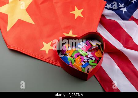 Rotes Herz voller Buchstaben in der Mitte einer chinesischen und US-Flagge auf einem grünen Tisch. Stockfoto