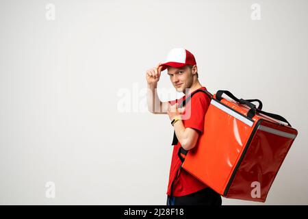 Junger Kurier mit Thermobeutel auf farbigem Hintergrund, Platz für Text. Lieferservice. Delivery guy in einem roten T-Shirt Uniform arbeiten als Kurier und Stockfoto