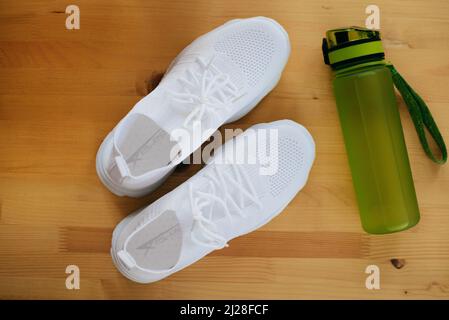 Weiße Sport-Sneakers mit grüner Wasserflasche auf Holzhintergrund Stockfoto