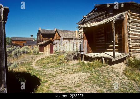 MT: Beaverhead County, Dillon Gegend, Bannack State Park (Geisterstadt), verlassene Blockhütten säumen eine grasvererstickte Straße. [Fragen Sie nach #170,070.] Stockfoto