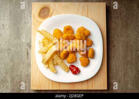 Hühnchen-Nuggets und pommes mit etwas Tomatensauce auf einem Teller auf einer Holzoberfläche, fertig zum Essen, schnelle Mahlzeit Stockfoto