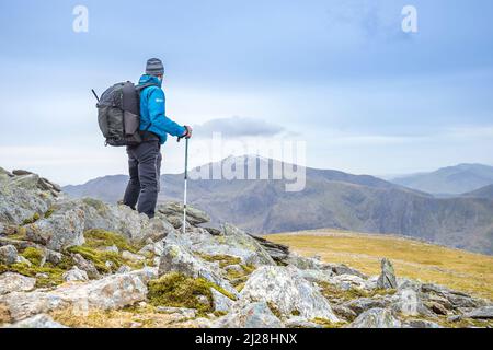 Rückansicht eines männlichen Wanderers mit Wanderstöcken und Rucksack auf einem wilden Camping-Abenteuer, der isoliert in den walisischen Bergen steht und Mount Snowdon, Wales, betrachtet. Stockfoto