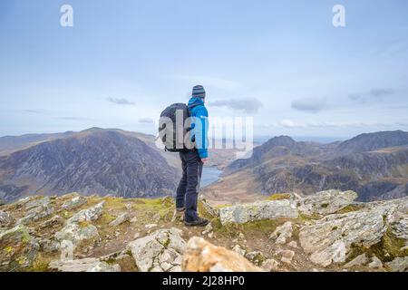 Rückansicht eines isolierten Wanderers mit Rucksack, der Anfang des Frühlings in den Bergen des Snowdonia National Park, North Wales, Großbritannien, unterwegs war. Stockfoto