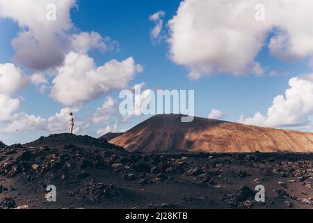 Frau, die sich mit den Händen in den Himmel erhebt und einen atemberaubenden Blick auf die vulkanische Landschaft im Timanfaya-Nationalpark auf Lanzarote, Spanien, genießt. Freiheit und Reisen Stockfoto