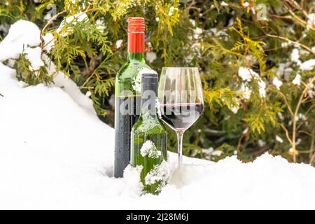 Zwei Flaschen Rot- und Weißwein mit einem Glas Rotwein im kalten Schnee Stockfoto