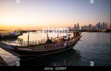 Doha, Katar. 30. März 2022. Ein Dhow-Boot mit Touristen fährt bei Sonnenuntergang von der Corniche-Promenade ab, um eine Tour vor der Skyline von West Bay Doha zu Unternehmen. Doha wird am 31. März den FIFA-Kongress und am 1. April die Auslosung der WM 2022 in Katar ausrichten. Quelle: Christian Charisius/dpa/Alamy Live News Stockfoto