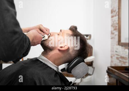 Junger Hipster kaukasischer Mann während der Bartpflege in einem modernen Friseurladen. Haarstyling für Männer. Schöner Mann immer neue Frisur mit elektrischen Trimmer. Hochwertige Fotografie Stockfoto