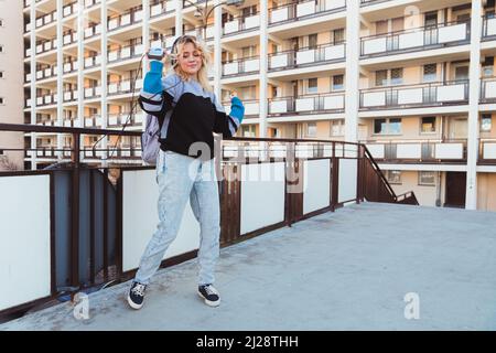 Vintage-inspiriertes junges kaukasisches Mädchen, das draußen in ihrem Bezirk mit altmodischem Musikgerät tanzt. 90s Konzept. Hochwertige Fotos Stockfoto