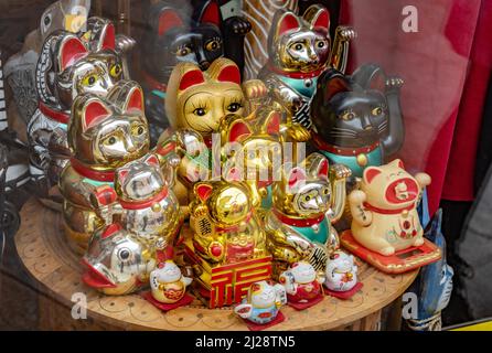 Übersetzung: 'Winkende Katze'. Mehrere traditionelle japanische Maneki Neko winkende Katze bewegliche Pfoten Figuren auf einem Geschäft Display, Gruppe von Objekten Stockfoto