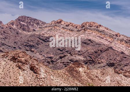 Nelson, Nevada, USA - 21. Mai 2011: Berge entlang des Eldorado Canyons zeigen Felsschichten in verschiedenen Farben unter blauer Wolkenlandschaft. Stockfoto