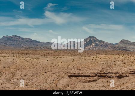 Nelson, Nevada, USA - 21. Mai 2011: Einfarbiger Wüstenbeige mit einigen kleinen grünen Büschen vor grauen Bergen unter blauer Wolkenlandschaft in Eldorado Stockfoto