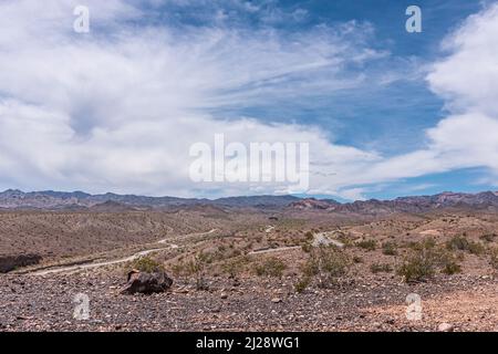 Nelson, Nevada, USA - 21. Mai 2011: Weite braune Wüstenlandschaft mit grünen Büschen unter blauer Wolkenlandschaft und Route 165 schlängelt sich durch sie. Stockfoto