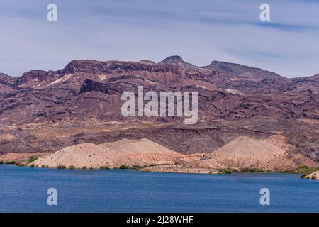 Nelson, Nevada, USA - 21. Mai 2011: Blauer Colorado River vorne mit der Küste von Arizona und seinen trockenen felsigen Hügeln und Bergen dahinter unter hellblau Stockfoto