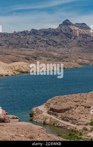 Nelson, Nevada, USA - 21. Mai 2011: Kleines Boot auf dem blauen Colorado River, das durch trockenes Wüstenland mit Bergen, Hügeln und einigen grünen Pflanzen auf sich zieht Stockfoto