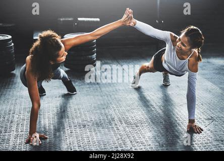Bringen Sie Ihren besten Freund und geben Sie ihm Ihr Bestes. Aufnahme von zwei jungen Frauen, die sich gegenseitig eine hohe fünf geben, während sie Liegestütze im Fitnessstudio machen. Stockfoto