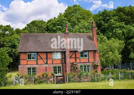 Außenansicht eines charmanten freistehenden Landhauses aus rotem Backstein im Sommer mit rosa Rosen im Dorf Shere, Surrey Hills, England, Großbritannien Stockfoto