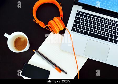 Willkommen in der Welt des modernen Business. Ein leerer Arbeitsbereich mit Laptop, Ohrhörern und Notebook ist in einem hohen Winkel aufgenommen. Stockfoto