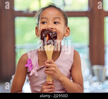 Der beste Morgen aller Zeiten. Aufnahme eines entzückenden kleinen Mädchens, das einen mit Schokoladenteig überzogenen Löffel leckt, während es zu Hause in der Küche bäckt. Stockfoto