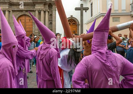 Gruppe von Bußregenten in purpurfarbenem Kostüm und Jesus Christus, der während der Karfreitag-Osterprozession in den Straßen von Quito, Ecuador, Kreuz trägt Stockfoto