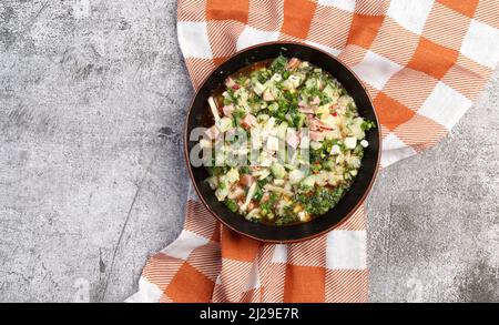 Traditionelle russische sommerliche kalte Suppe Okroshka mit Wurst, Gemüse und Kvass in einer Schüssel auf dunkelgrauem Hintergrund. Draufsicht, flach liegend Stockfoto