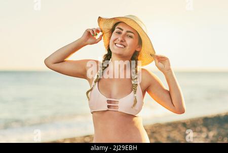 Ich brachte meinen Hut, um mich vor der Sonne zu schützen. Aufnahme einer jungen schönen Frau am Strand. Stockfoto