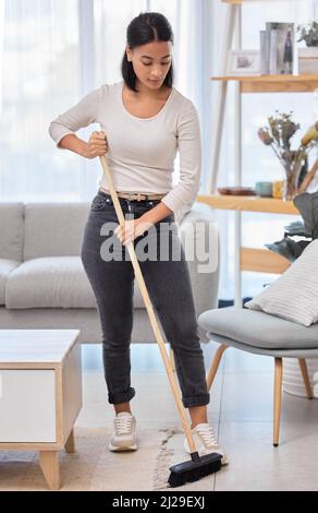 Fegen Sie es einfach unter den Teppich. Aufnahme einer jungen Frau, die zu Hause den Boden fegen soll. Stockfoto