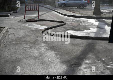 Ein dicker Schlauch wird in einen offenen Wasser- oder Kanalisationsbrunnen abgesenkt. Reparatur- und Renovierungsarbeiten in einem Wohngebiet der Stadt. Roter Holzzaun in installiert Stockfoto