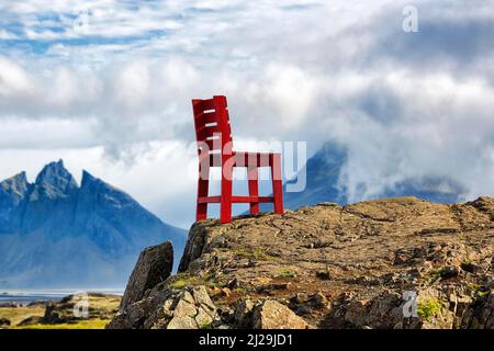 Roter Holzstuhl auf einem Felsen, Blick auf Mount Brunnhorn, Klifatindur Bergkette im Sommer, Ostisland, Island Stockfoto