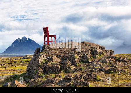 Roter Holzstuhl auf einem Felsen, Blick auf Mount Brunnhorn, genannt Batman Mountain, Klifatindur Bergkette im Sommer, Ostisland, Island Stockfoto