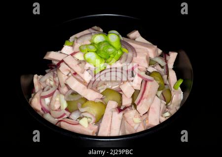 Wurstsalat mit roten Zwiebeln, Knoblauch und Gurken, Studiofotografie mit schwarzem Hintergrund Stockfoto