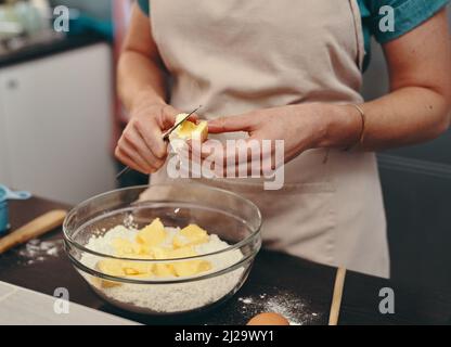 Backen ist nicht nur ein Hobby, sondern eine Leidenschaft. Ausschnitt einer unkenntlichen Frau, die zu Hause in ihrer Küche Backblöcke geschnitten hat. Stockfoto