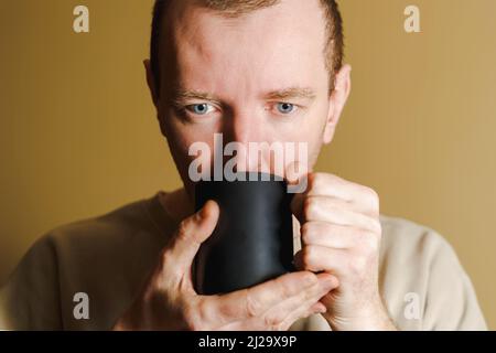 Porträt eines Mannes, der Kaffee aus einer schwarzen Tasse trinkt. Stockfoto