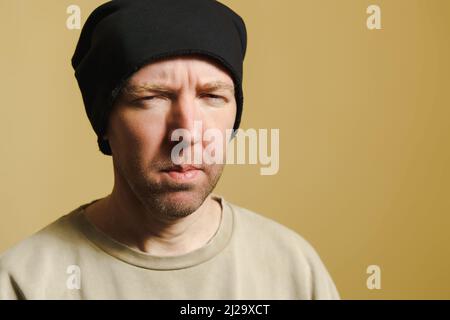 Der Mann im schwarzen Hut sieht verdächtig aus. Porträt eines jungen Mannes, der Gesichter macht. Stockfoto