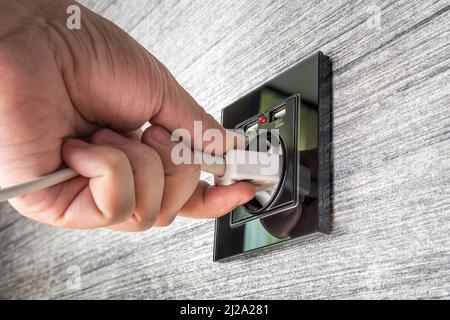 Hand Putting Plug in Electricity Modern Socket. Anschluss an die Stromversorgung an der Wand aus einer Steckdose. Stockfoto