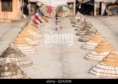 Brahmanbaria, Chittagong, Bangladesch. 31. März 2022. Kinder laufen und spielen zwischen Hunderten traditioneller Reismühlen aus Bambus.nach dem Kochen wird das Getreide von Arbeitern in Haufen gefegt und bis zu acht Stunden lang in Brahmanbaria, Bangladesch, getrocknet. Die Reismühlenarbeiter begannen ihre Arbeit von sehr früh morgens von 5 bis 2pm Uhr täglich. Nach der Mittagspause spielen die Kinder der Arbeiter ihre Nachmittagsspiele mit Freunden in diesem Reismühlenfeld. (Bild: © Mustasinur Rahman Alvi/ZUMA Press Wire) Bild: ZUMA Press, Inc./Alamy Live News Stockfoto