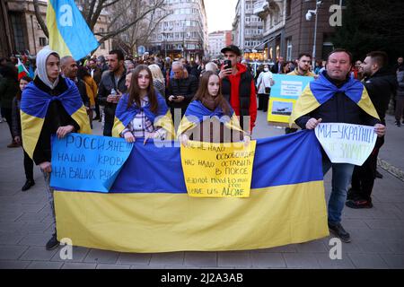 Sofia, Bulgarien - 24. März 2022: Während einer Demonstration zur Unterstützung der Ukraine einen Monat nach Ru halten Menschen Protestschilder und die ukrainische Nationalflagge Stockfoto