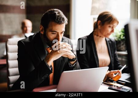Geschäftsmann mit zusammengeklemmten Händen und Blick auf den Laptop, der von einer Geschäftsfrau am Schreibtisch in der Anwaltskanzlei gearbeitet wird Stockfoto