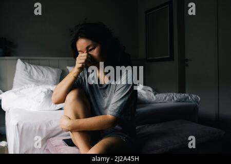 Traurige Frau weinte, während sie zu Hause auf der Bettbank im Schlafzimmer saß Stockfoto