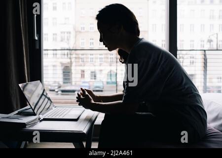 Seitenansicht einer Frau, die einen Laptop benutzt und im Schlafzimmer zu Hause sitzt Stockfoto