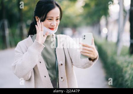 Asiatische Frau zieht ihre Gesichtsmaske aus, um ihr Telefon zu benutzen Stockfoto