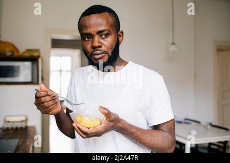 Nachdenklicher Mann schaut weg, während er alleine zu Hause isst Stockfoto