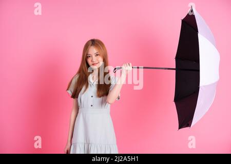 Junge asiatische Frau mit Regenschirm auf rosa Hintergrund Stockfoto