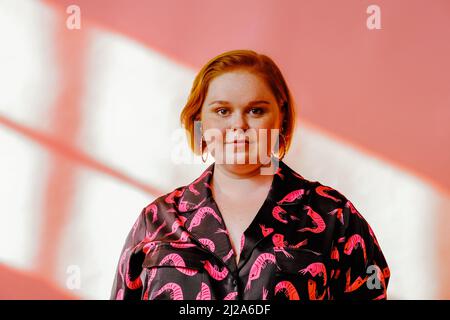 Lächelnde junge Frau posiert im Studio über rosafarbenem rothaarigen Hintergrund Stockfoto