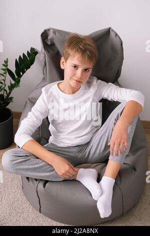 Blonde entspannte stilvolle Teenager sitzen auf einem Stuhl mit Sitzsack zu Hause. Weißes T-Shirt-Modell Stockfoto