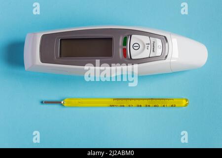 Zwei Thermometer aus verschiedenen Epochen, ein Quecksilber- und eines mit LED-Display und Lasertechnologie, zusammen auf einem farbenfrohen strukturierten Hintergrund. Gesundheitsfahrzeug Stockfoto