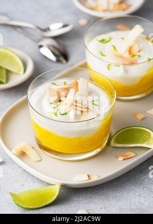 Gesundes tropisches Frischkäse-Dessert mit Mango-Püree und gerösteten Kokosnusschips in einem Glas. Vegan gesundes Frühstück. Stockfoto
